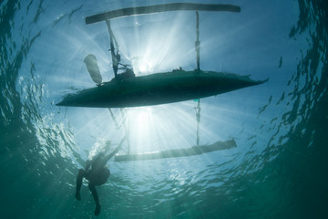 Wall Mural - An outrigger canoe is silhouetted by bright sunlight in North Sulawesi, Indonesia. Millions of people make their living by utilizing marine resources.