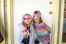 Two Young Girls Smiling And Wearing Colorful Masks.