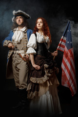 Wall Mural - Man in form of officer of United States War of Independence and girl in historical dress of 18th century. July 4 is US Independence Day. Studio photo on black background