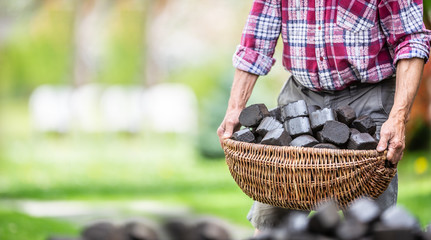 Man carrying basket full of coal briquettes in the backyard of his house