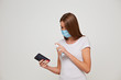 © Ryzhkov Oleksandr - Young woman in medical mask washes her mobile phone with a gel antiseptic spray. Conceptual photo on the theme of the epidemic.