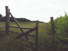 Open Wooden Gate Entrance Of Green Farm Field Against Sky