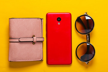 Wall Mural - Women's accessories and gadgets on a yellow background. Wallet, stylish round sunglasses, smartphone on a yellow background