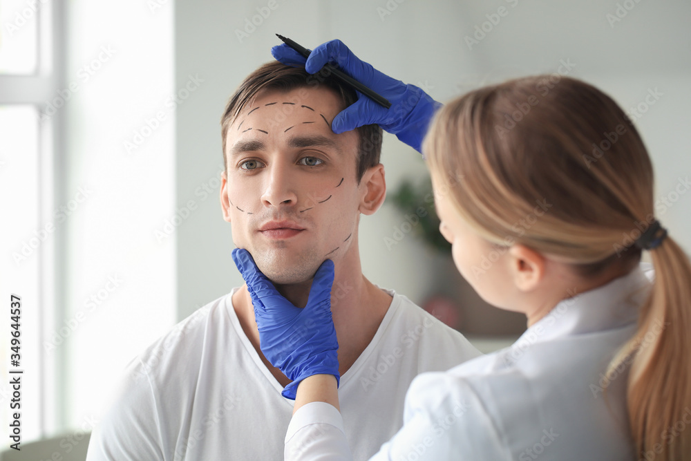 Plastic surgeon applying marks on man's face in clinic