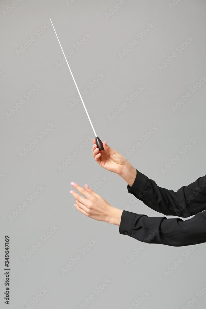 Hands of young female conductor on grey background