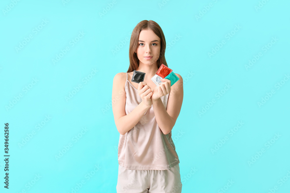Young woman with condoms on color background