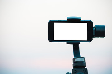 A mobile phone or smart phone with a white screen is equipped with a gimbal, a vibration stabilizer device for helping to shoot still videos.