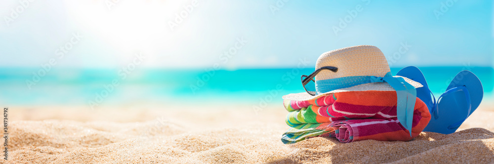 Beach accessories straw hat, flip flops, towel on sunny tropical beach, summer holidays vacation, Caribbean beach with turquoise water background - obrazy, fototapety, plakaty 