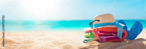 Fototapeta na drzwi i meble Akcesoria plażowe słomkowy kapelusz, klapki, ręcznik na słonecznej tropikalnej plaży, letnie wakacje, karaibska plaża z turkusową wodą w tle