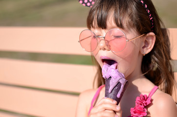 closeup of pretty little girl eating ice cream outdoors on sunny day. cute girl in pink swimsuit lic