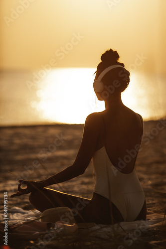 Plakaty elektroniczna muzyka  kobieta-w-pozycji-medytacji-jogi-ze-sluchawkami-na-plazy