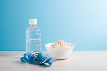 bottle of water, a bowl of boiled oatmeal and blue measuring tape on a wooden table, proper nutrition concept, healthy breakfast, blue background, copy place