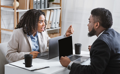 Annoyed black woman quarelling with her coworker at workplace, empty space