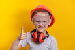Cute boy in builder glasses, helmet and headphone to ear protection shown big finger up over yellow background  copy space
