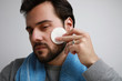 © face_reader_img - Close-up of handsome bearded man with blue towel using cotton pad while cleaning his skin.