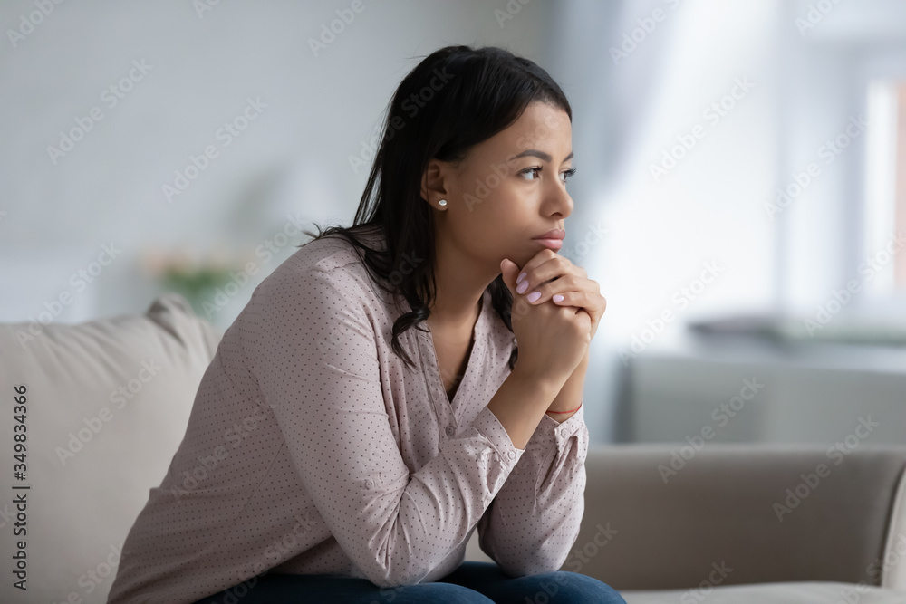 Concerned sad African woman sit on sofa in living room thinking of problem looks in distance feels depressed due loneliness, inner emptiness, life troubles, break up or divorce, marriage split concept - obrazy, fototapety, plakaty 