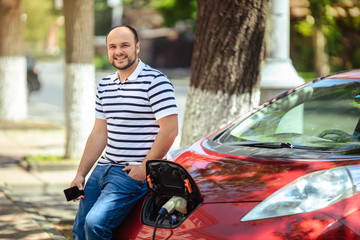 Caring for the environment. A man connects a charger to an electric car in the city.