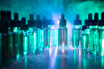 Smoke clouds and vape liquid bottles on dark background. Light effects. Useful as background or vape advertisement or vape background. Selective focus