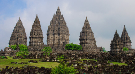 Ancient stone ruins on green field and Candi Prambanan or Rara Jonggrang, Hindu temple compound on background. Impressive architectural site. Yogyakarta, Central Java, Indonesia. 