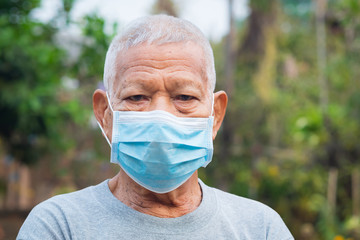 A portrait of an elderly man wearing a face mask looking at camera while standing in a garden. Mask for protect virus, coronavirus, pollen grains. Concept of old people and healthcare