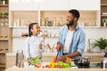 Wall Mural - Friendly little girl and her daddy making veggies salad together