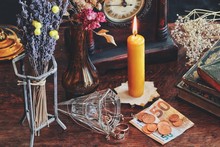 A Money Spell On A Witch Altar. Slightly Blurred Background With A Focus On Money Banknotes And Coins Next To Vintage Golden Jewelry On A Table. Yellow Gold Colored Candle Lit In The Background