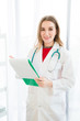 © Masato - Female beautiful wearing a doctor uniform have a stethoscope and holding a green paper chart and smiling.