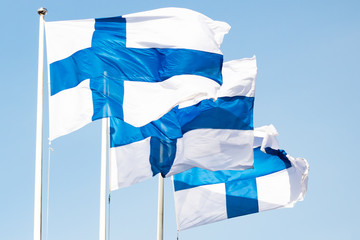 Three finnish national flags on the wind against the blue sky