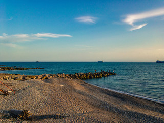 Wall Mural - Pebble beach with breakwaters against the background of the turquoise sea and the blue cloudy sky.