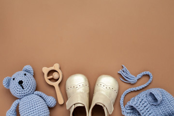 Flat lay composition with baby accessories set: crib shoes, teddy bear toy, knitted hat, wooden rattle and copy space.