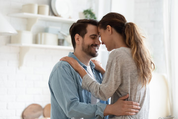 Wall Mural - Happy millennial husband and wife hug cuddle enjoy tender romantic moment in kitchen, smiling loving young couple embrace on domestic date at home, having romance together, relationships concept