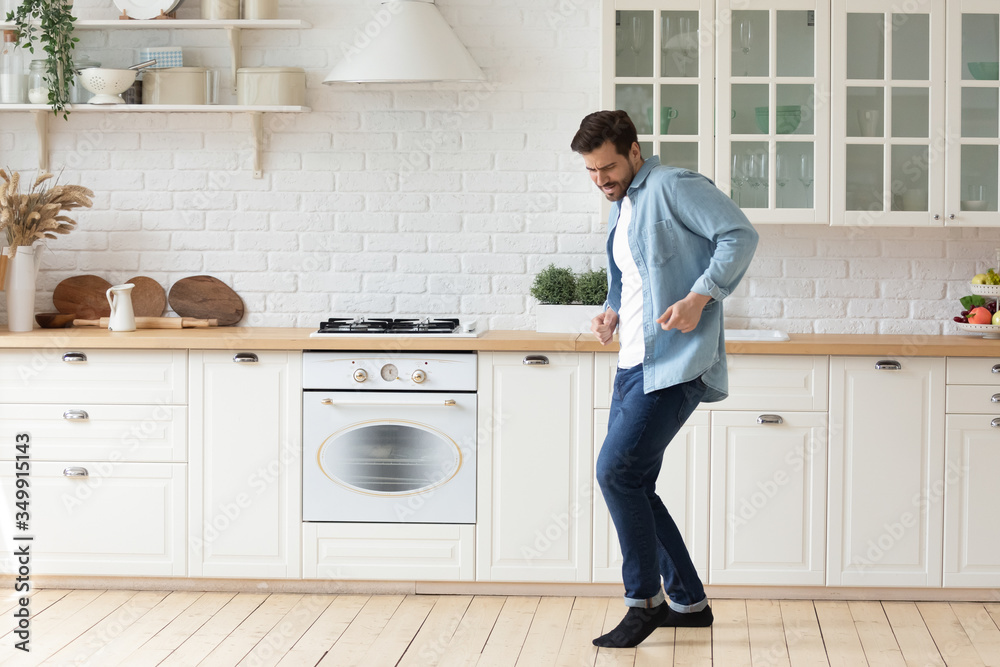 Happy millennial man enjoy leisure weekend dancing alone in bright modern design white kitchen, overjoyed young husband have fun entertain celebrate moving to new own home or apartment - obrazy, fototapety, plakaty 