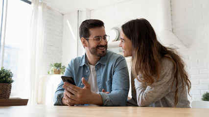 overjoyed husband and wife sit at table in modern design kitchen laugh enjoy family weekend using mo