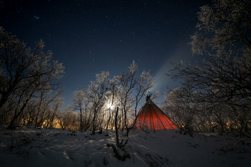 arctic camp site at night with moon and smoking tent with snow covered trees around