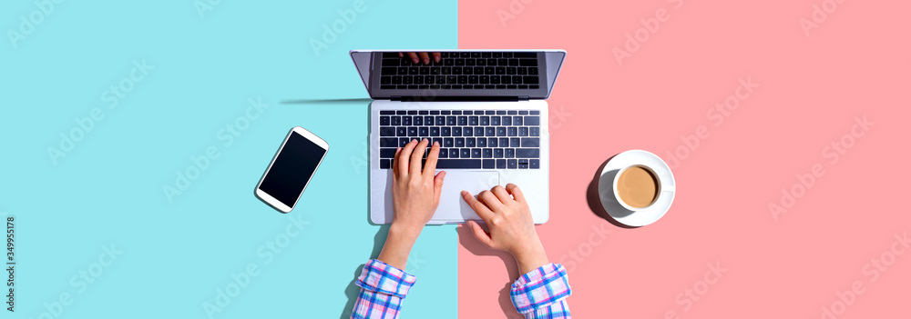Woman using a laptop computer with a phone and a cup of coffee - obrazy, fototapety, plakaty 