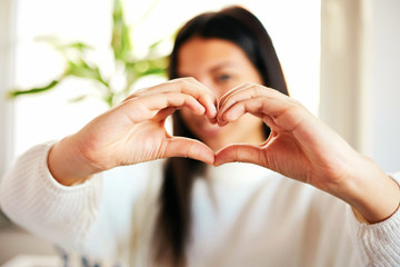 Beautiful teenage Asian girl making heart shape with hands in her room.