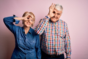 Wall Mural - Senior beautiful couple standing together over isolated pink background doing ok gesture with hand smiling, eye looking through fingers with happy face.