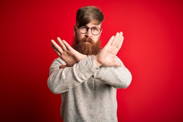 Sticker - Handsome Irish redhead man with beard wearing casual sweater and glasses over red background Rejection expression crossing arms doing negative sign, angry face