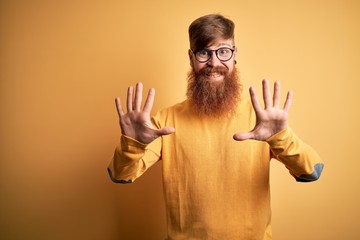 Canvas Print - Handsome Irish redhead man with beard wearing glasses over yellow isolated background showing and pointing up with fingers number ten while smiling confident and happy.