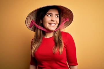 Canvas Print - Young blonde woman wearing traditional asian rice paddy straw hat over yellow background looking away to side with smile on face, natural expression. Laughing confident.