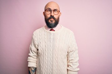 Sticker - Handsome bald man with beard and tattoo wearing glasses and sweater over pink background making fish face with lips, crazy and comical gesture. Funny expression.