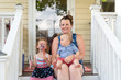 Young mom sitting on the front porch with two toddler children on the 4th of July