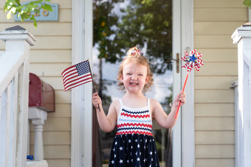 Happy toddler girl waving a flag and a pinwheel on the Fourth of July