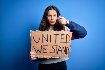 Sticker - Beautiful activist woman holding banner with united stand message over blue background pointing with finger to the camera and to you, hand sign, positive and confident gesture from the front