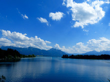 Scenic View Of Blue Lake In Front Of Mountains Against Cloudy Sky
