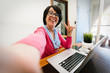 © Davide Angelini - Mature older woman taking a selfie at home using computer technology.