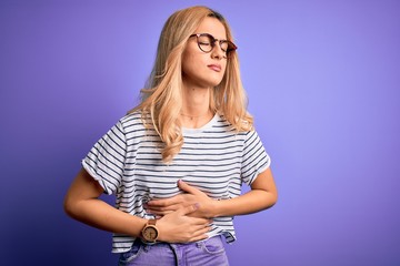 Canvas Print - Young beautiful blonde woman wearing striped t-shirt and glasses over purple background with hand on stomach because indigestion, painful illness feeling unwell. Ache concept.