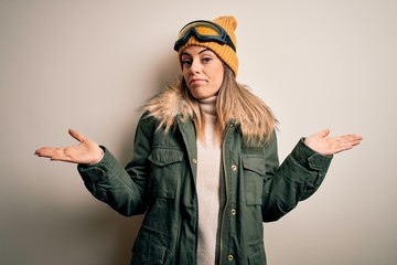 Canvas Print - Young brunette skier woman wearing snow clothes and ski goggles over white background clueless and confused with open arms, no idea concept.