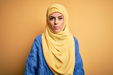 Poster - Young beautiful brunette muslim woman wearing arab hijab over isolated yellow background Relaxed with serious expression on face. Simple and natural looking at the camera.