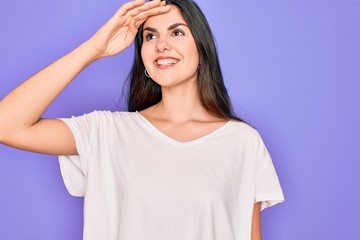 Sticker - Young beautiful brunette woman wearing casual white t-shirt over purple background very happy and smiling looking far away with hand over head. Searching concept.